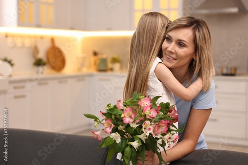 Little daughter congratulating her mom with bouquet of alstroemeria flowers in kitchen, space for text. Happy Mother's Day
