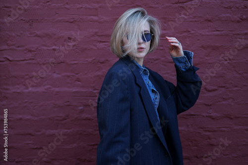 Blond hair model wearing sunglasses in front of purple brick wall photo