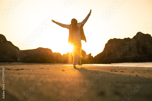 carefree woman walking on the beach at sunset with arms up photo
