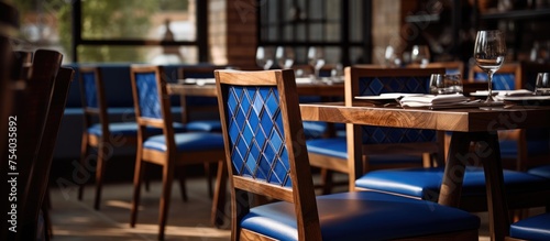 A restaurant setting with wooden tables and chairs in a calming blue hue. The chairs are neatly arranged around the tables, creating a welcoming dining environment.