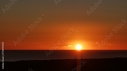 Il Sole accecante che all’alba sorge dal mare visto da sopra le colline 