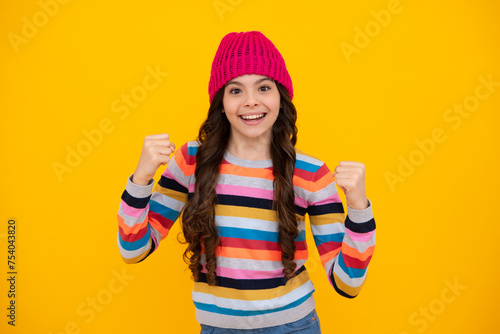 Modern teenage girl 12, 13, 14 year old wearing sweater and knitted hat on isolated yellow background. Happy teenager, positive and smiling emotions of teen girl.