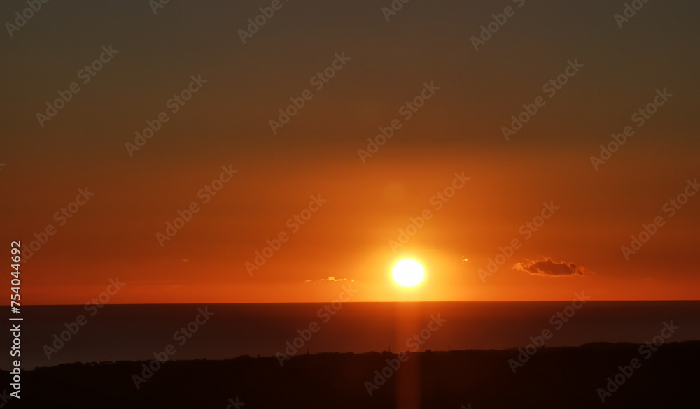 Fototapeta premium Il Sole accecante che all’alba sorge dal mare visto da sopra le colline 