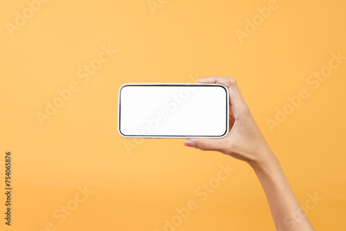 Hand holding blank smartphone in landscape mode for mockup isolated on yellow background