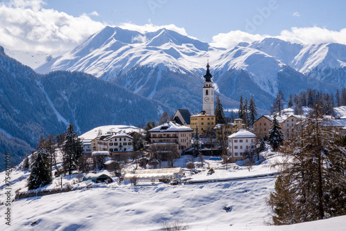 Alpine mountain panorama in winter. Beautifully located mountain village of Ftan in Engadine, Switzerland. Snow-capped mountain peaks and white clouds against a blue sky
