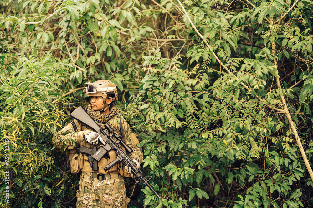 In the bushes, American soldiers are camouflaged from enemies, carrying M16 pistols, wearing military uniforms, helmets, and vision goggles in a dangerous battlefield from terrorists.