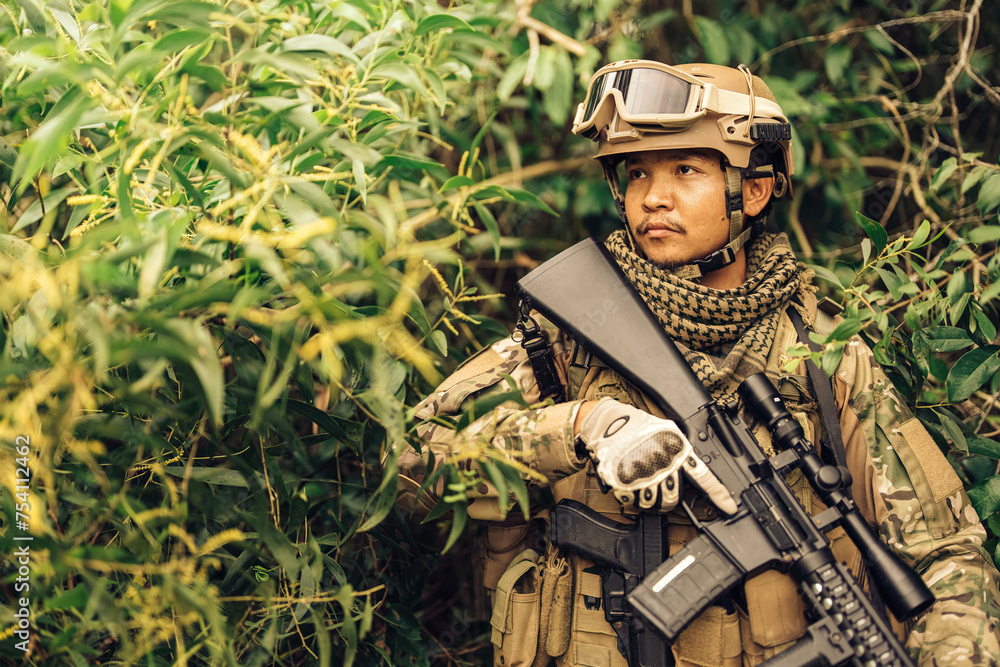 The SEAL leader holds an M16 rifle ready to fire, hides in the bushes, listens to the sound of enemy footsteps around him, and engages in the dangerous battlefield of the army's military battles.