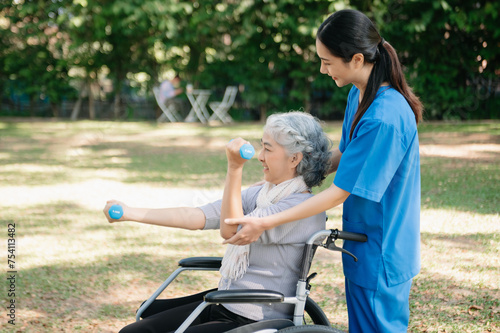 Asian physiotherapist helping elderly woman patient stretching arm during exercise correct with dumbbell in hand during training hand with patient Back problems in the garden. © laddawan