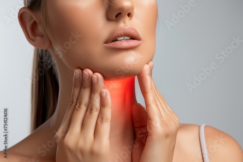 Female checking thyroid gland by herself. Close up of woman in white t- shirt touching neck with red spot. Thyroid disorder includes goiter, hyperthyroid, hypothyroid, tumor or cancer. Health care