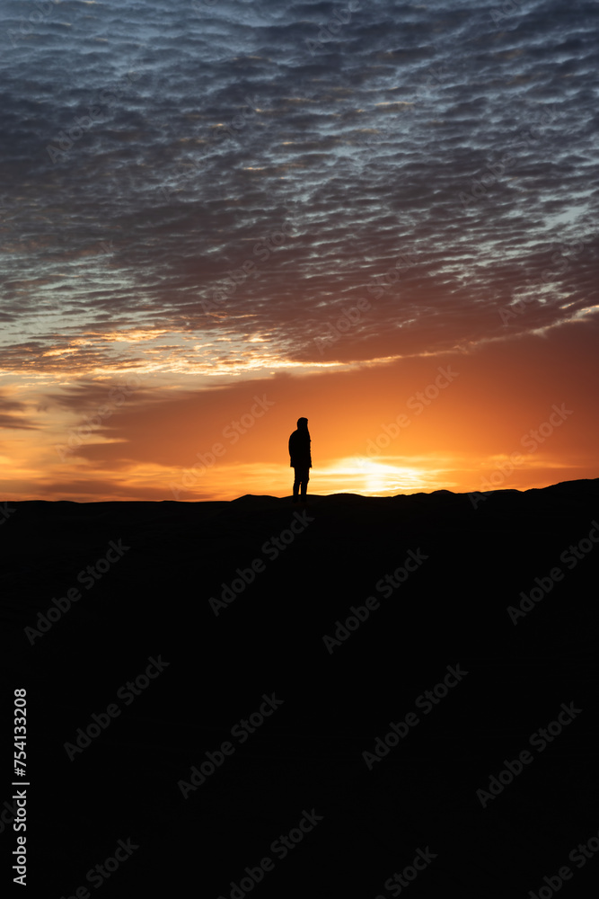 Silhouette of a person watching the sunrise on a dune in the desert of Morocco