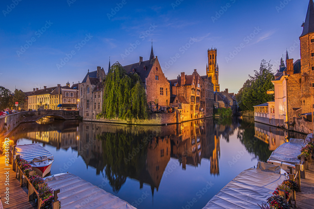Canal of the Rosary Quay in the Hanseatic city of Bruges in the evening. Reflection on the water surface of the historic buildings. Belfry of the old town and historic guild houses and merchant houses