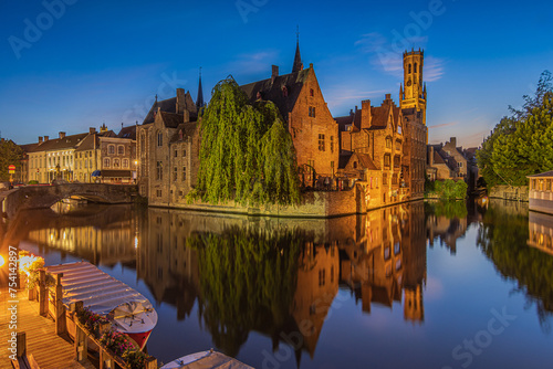 Center of old town Bruges. Belgian Hanseatic city in the evening with the Rosary Quay canal at blue hour. Reflections on the water surface. Old illuminated merchant houses with belfry