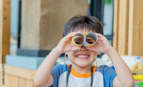 Little asian boy making tissue paper core binoculars. Reuse waste products. Idea custom made toy. Soft focus. Copy space.