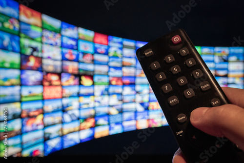 Man using remote control to watch a movie streaming service on TV. Video-on-demand subscription service and platform on television. Stream series, films and shows online.