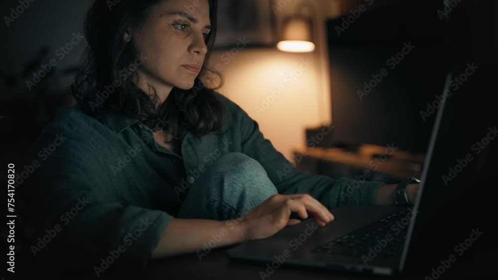 A tired young woman is working on a laptop while sitting in the living room late at night. A tired young woman is working on a laptop while sitting in the living room late at night.