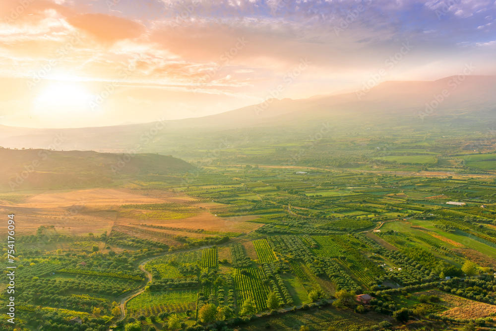 scenic rustic landscape with green hills and farms in a mountain valley during colorful cloudy sunset