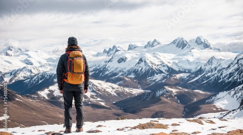 Mountaineer admiring snowy peaks under a cloudy blue sky 