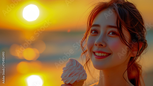 Beautiful smiling young  Chinese / Japanese Asian woman eating an ice cream on a beach with the sea in the background at sunset. © robert