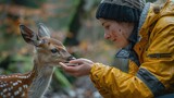 A gentle scene at an animal sanctuary where a volunteer tenderly feeds a rescued baby deer, surrounded by a lush, serene forest backdrop, highlighting the connection between humans and wildlife