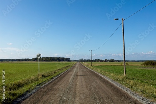 Rural gravel road between agricultural fields in summer, Ruotsinkylä, Ruotsinpyhtää, Finland.