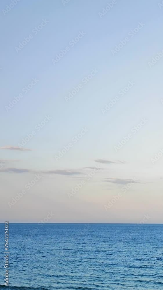 White clouds on the blue sky above the surface of the blue sea. Seascape. Sea view. Natural background. Nature backdrop. Vibrant bright sea scenery. Vertical White clouds on the blue sky above the surface of the blue sea. Seascape. Sea view. Natural background. Nature backdrop. Vibrant bright sea scenery. Vertical