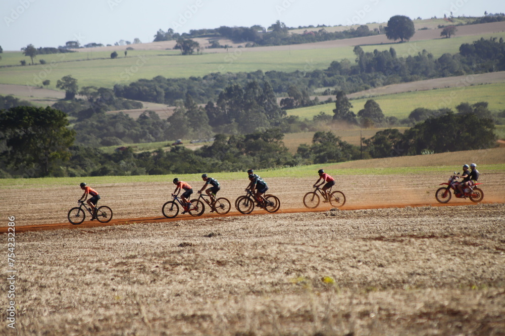 Obraz premium Palha de colheita de soja, ciclistas passando, e árvores ao fundo.