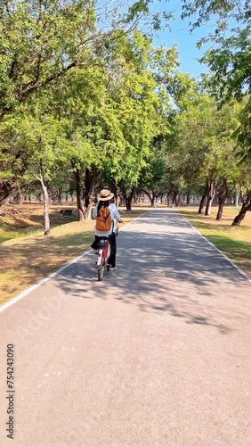 Wallpaper Mural A woman is on a bike riding along an asphalt path in a park, passing by trees and grass. The wheels are rolling smoothly on the road surface in Sukhothai Thailand Torontodigital.ca