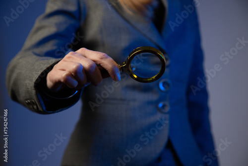 Business woman holding a magnifying glass in her right hand on a gray background. No face. Blue color correction