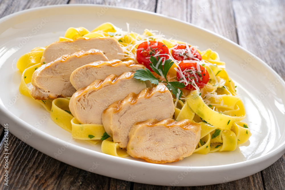 Grilled sliced chicken breast and pappardelle noodles on wooden background
