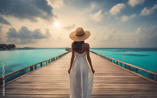 Traveler woman seen from behind wearing hat and dress walking over wooden bridge on Maldives resort.