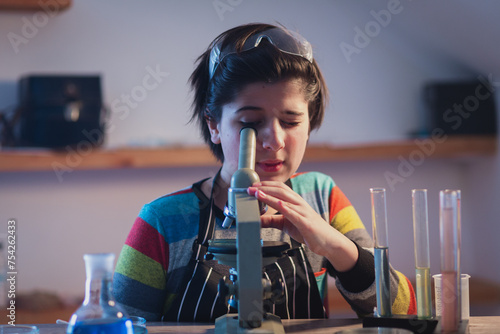 Hobbies and free time. Modern educational program including practical classes. A young researcher in a home laboratory wearing safety glasses works intently with a microscope.