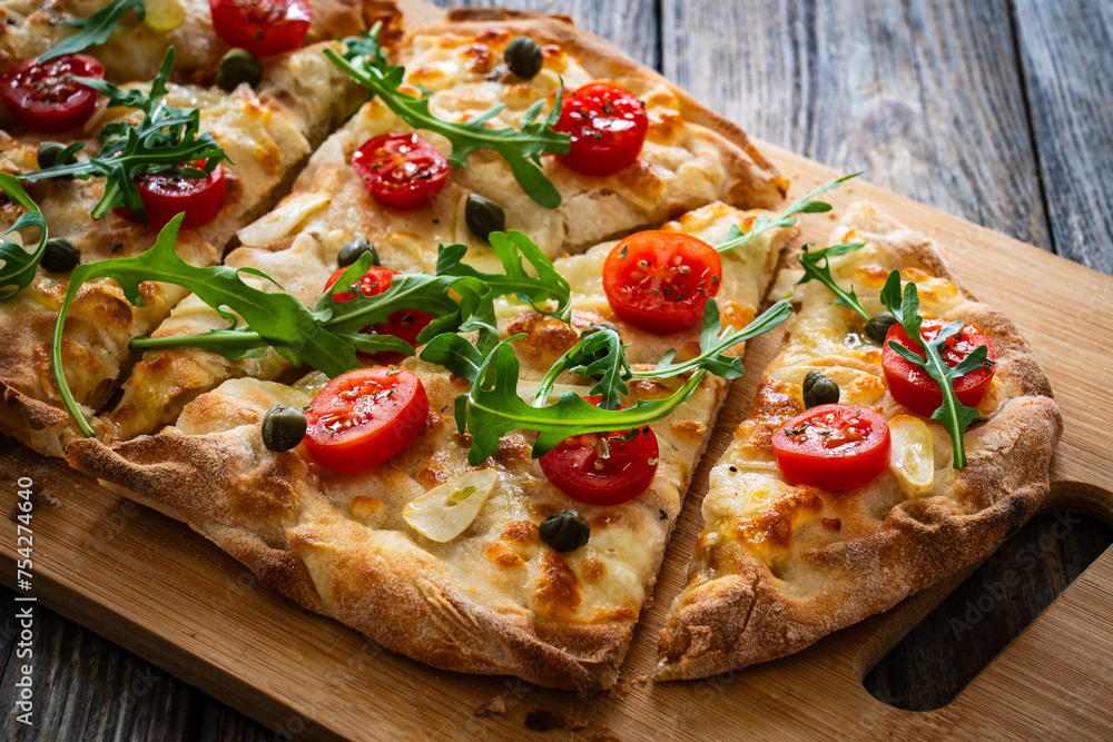 Roman pinsa with mozzarella cheese, capers, arugula and garlic on wooden table
