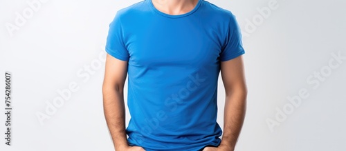 A man wearing a blue shirt and jeans is striking a pose for a picture on a white background. He looks relaxed and confident as he poses.