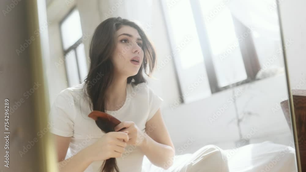 Portrait of nervous brunette young woman having difficulty brushing her tangled hair dryness split ends problem by wooden brash while looking at mirror reflection at home Portrait of nervous brunette young woman having difficulty brushing her tangled hair dryness split ends problem by wooden brash while looking at mirror reflection at home
