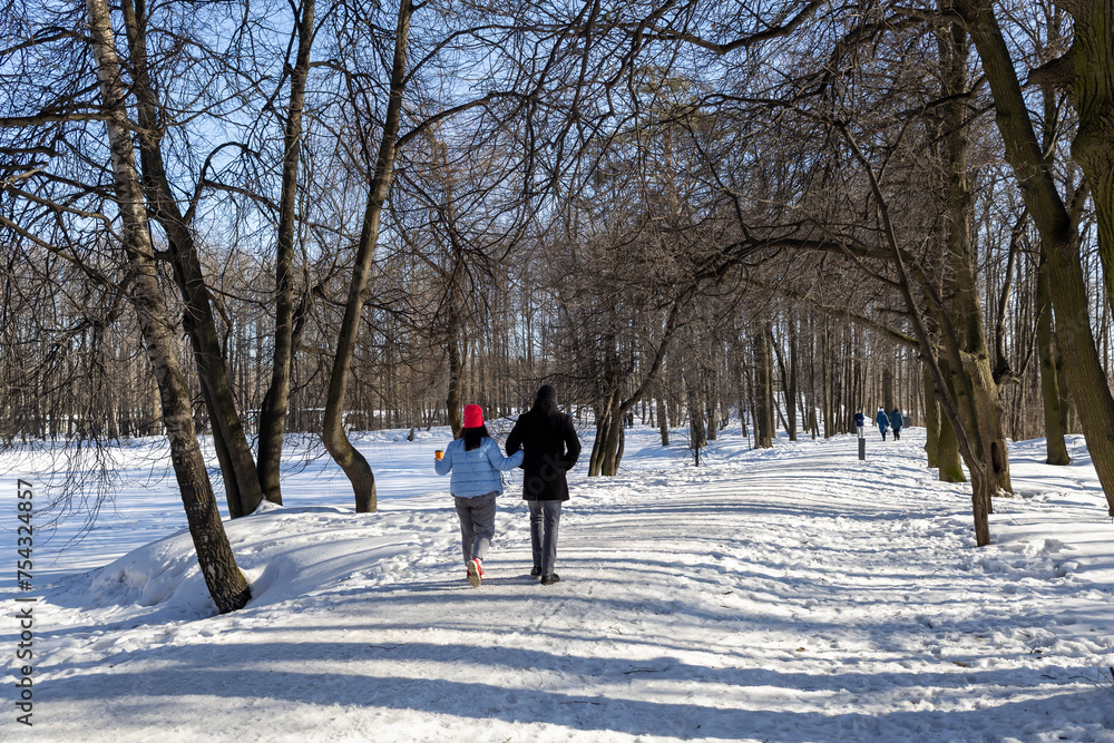 A young couple strolls through the park on a bright winter day. Winter walk. A young couple strolls through the park on a bright winter day. Winter walk.