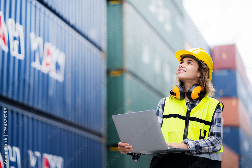 A woman wearing a yellow vest and a hard hat is holding a laptop. She is smiling and she is happy A woman wearing a yellow vest and a hard hat is holding a laptop. She is smiling and she is happy