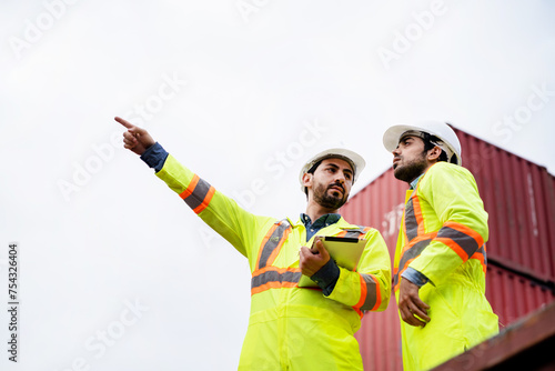 Two men in yellow safety vests pointing at something. One of them is holding a clipboard. Scene is serious and focused