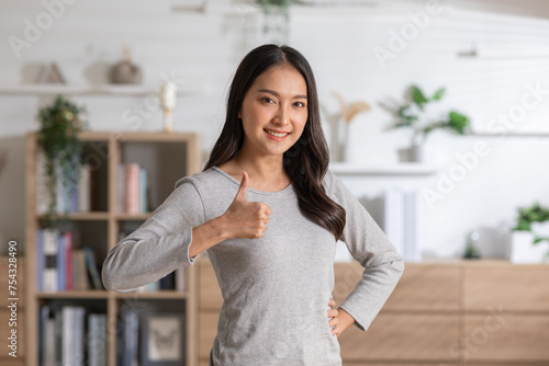 Smiling young woman giving a thumbs up sign, looking positive and confident at home