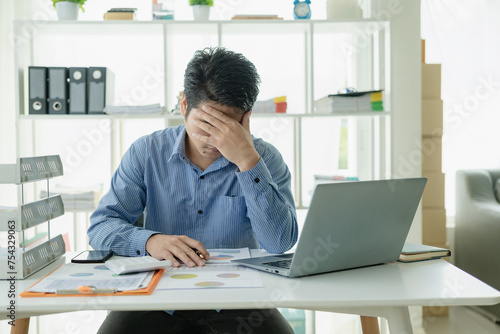 Business concept of a businessman with a headache while working sitting stressed at a desk with a laptop in the office touching his head. Entrepreneurs face problems with their businesses.