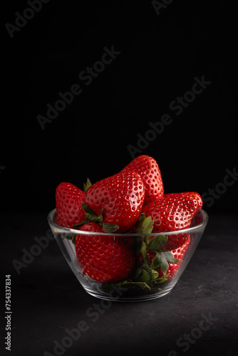 a glass bowl with delicious red strawberries on a black background