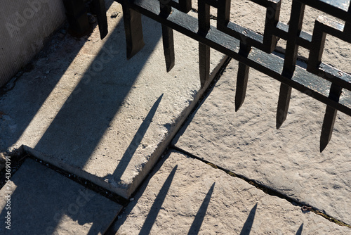 bottom of a wrought iron fence with sunlight and abstract shadows on squarish pavers photo