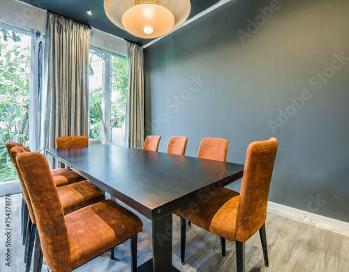 Meeting room or dinning area with large black table and 6 beige orange brown terracota chairs. Empty wall in taupe gray painting color. Luxury interior design home diningroom or restaurant photo