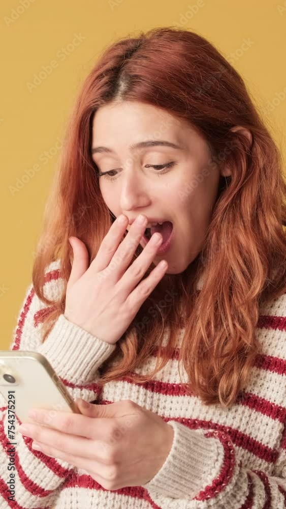 Surprised girl making choose using mobile app on yellow background Surprised girl making choose using mobile app on yellow background