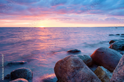 Magenta sunset over sea with stones and smooth water