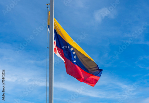 Venezuelan flag on a flagpole against a blue sky Venezuelan flag flutters in the wind against a sky with clouds
