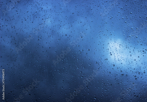 Rain drops on the window surface, dark blue clouds visible through the rain. Rainy background