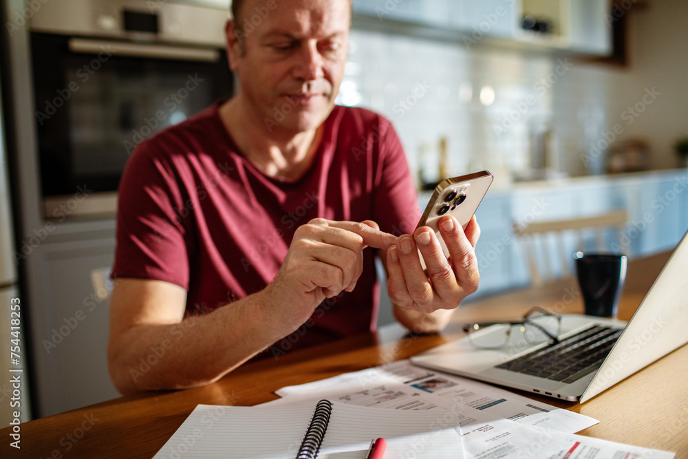 Close-up of a man using a smartphone with a laptop and documents on the table Close-up of a man using a smartphone with a laptop and documents on the table