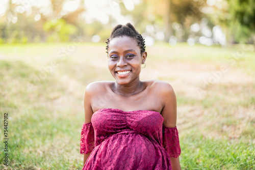 Happy African pregnant woman smiling on camera in a public park - Maternity lifestyle concept