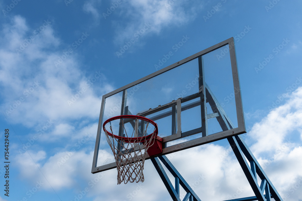 Basketball hoop with a transparent backboard against a blue cloudy sky