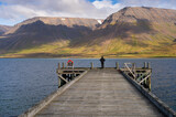 Girl standing at the edge of Önundarfjörður Pier and looking at beautiful view over fjord and mountains in Westfjords, Iceland